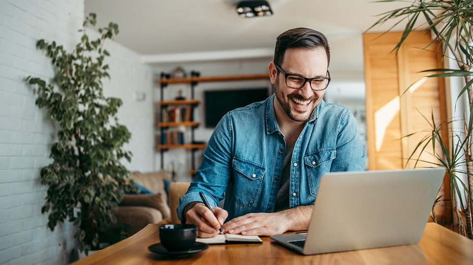 Man smiles and takes notes while working on computer